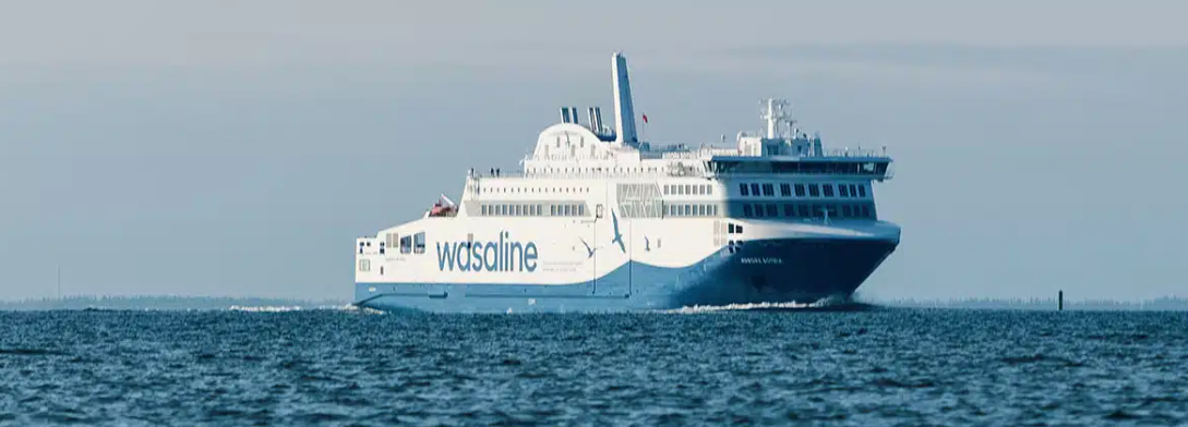 En stor vit och blå Wasaline-färja färdas över ett lugnt vattendrag under en klar himmel.